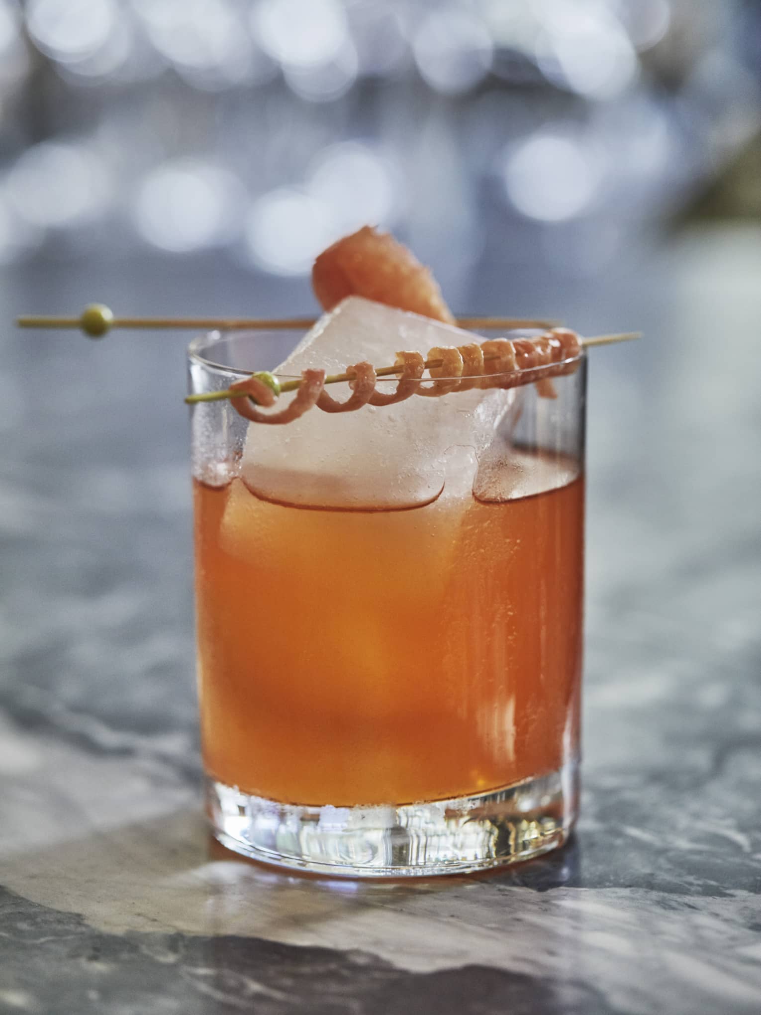 A cocktail with geometric ice and a decorative curled rind on a marble countertop