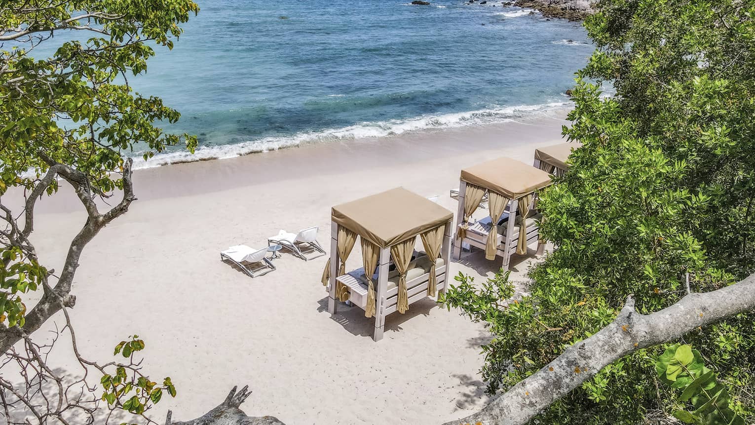 Cabanas and lounge chairs on a beach, with blue-green ocean and clear blue sky in the background
