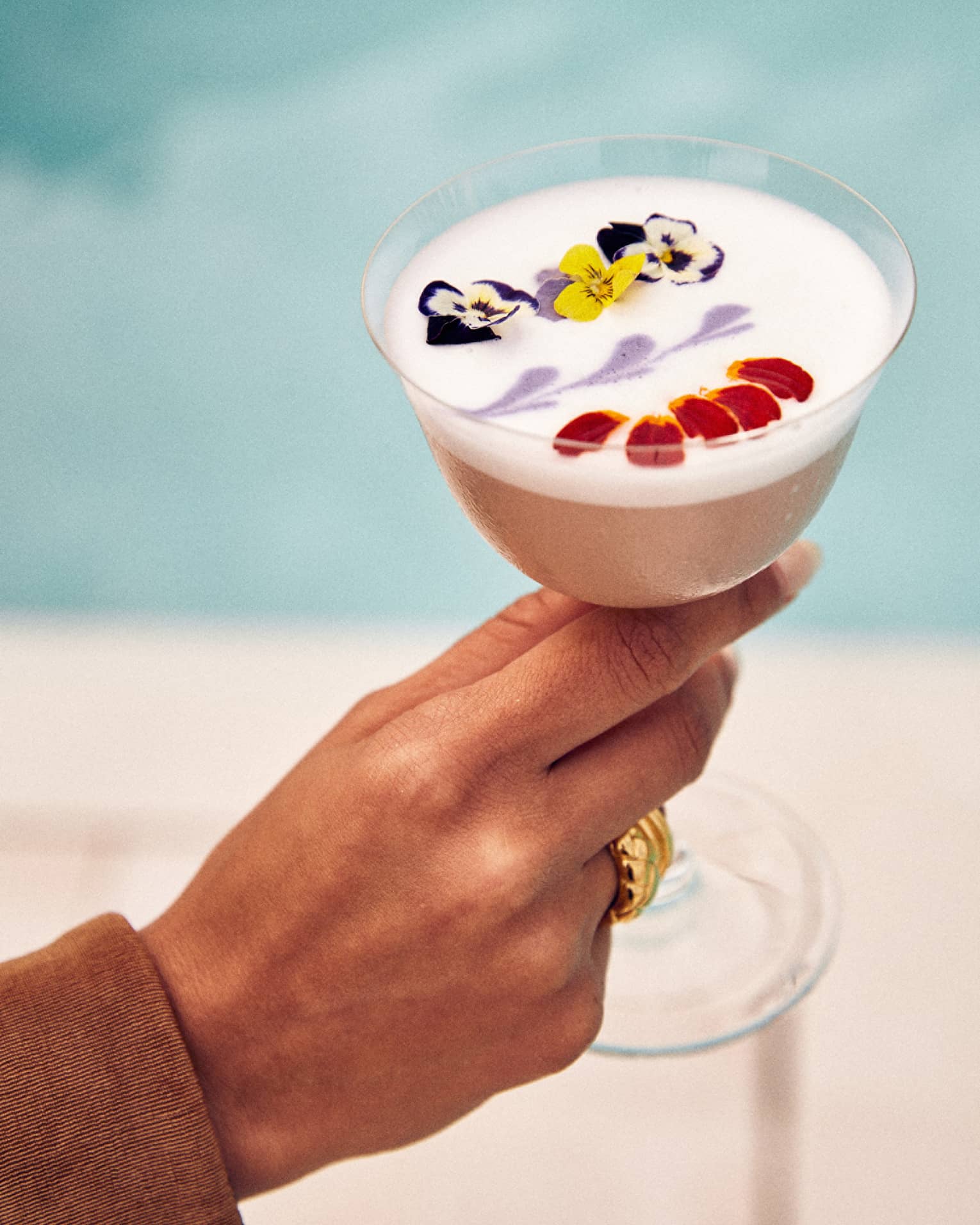 An egg white cocktail decorated with edible yellow, purple and white flowers, along with red petals and purple art on top.