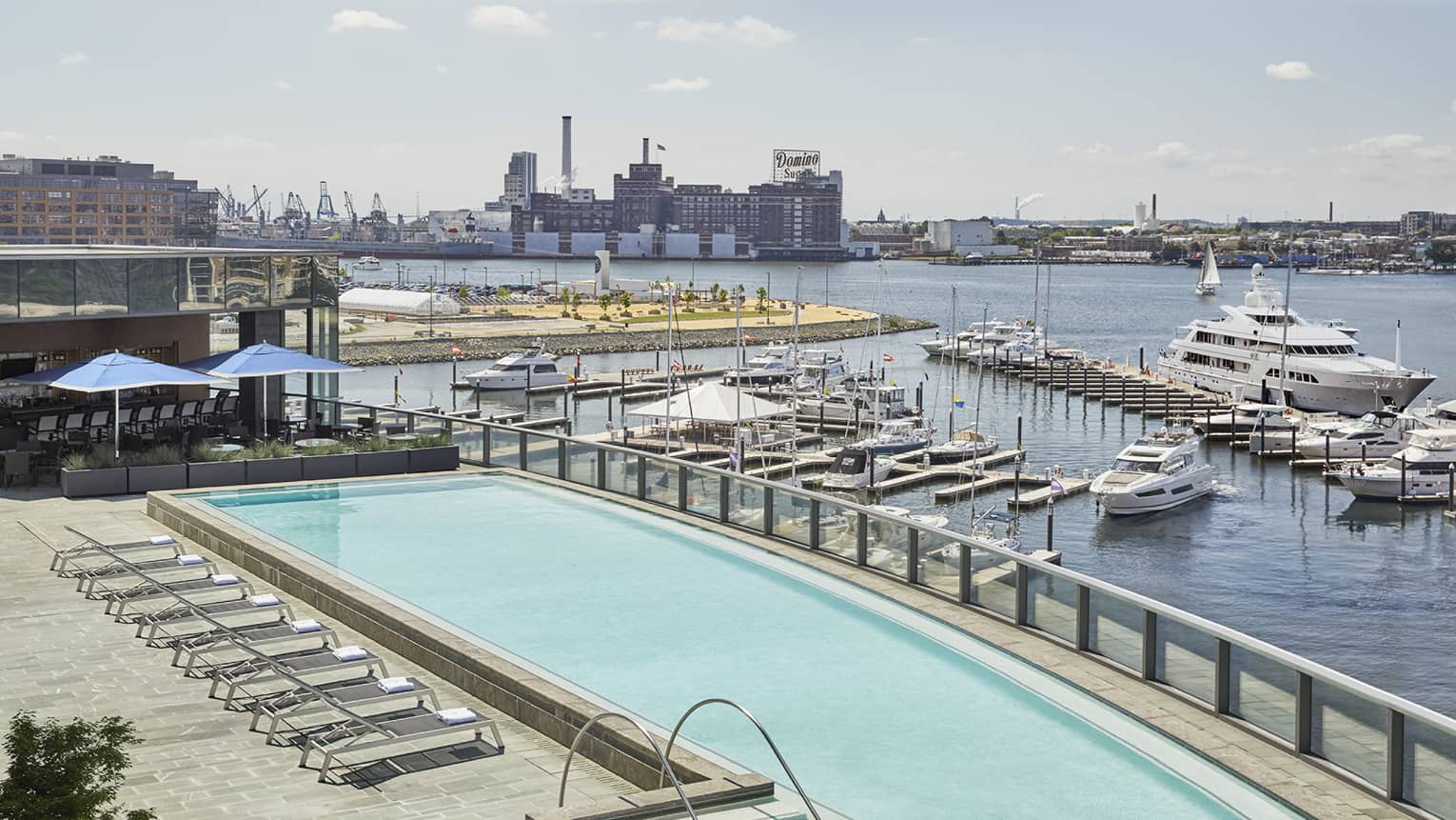 View over large outdoor swimming pool on patio by harbour with boats