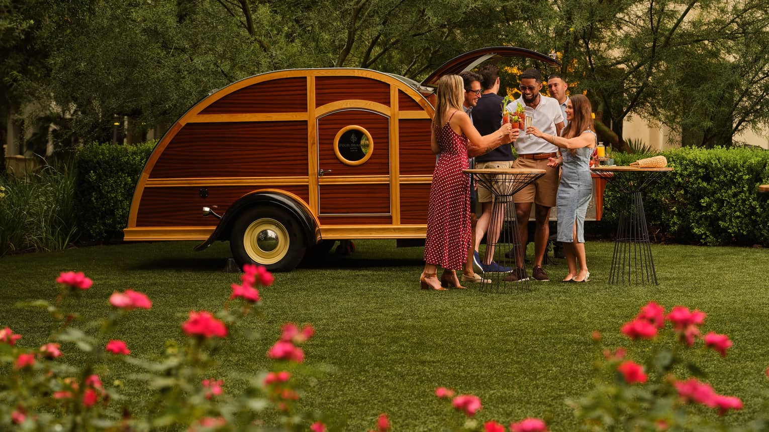 Many guests holding drinks and standing beside an outdoor camper