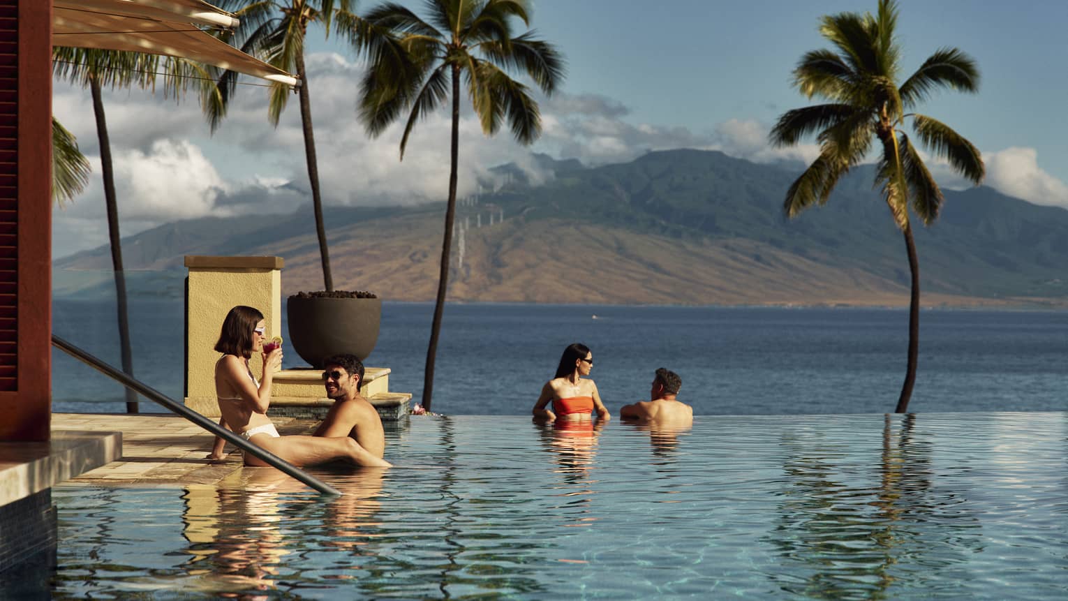 People relaxing in an infinity pool, enjoying ocean and mountain views at a Four Seasons luxury resort