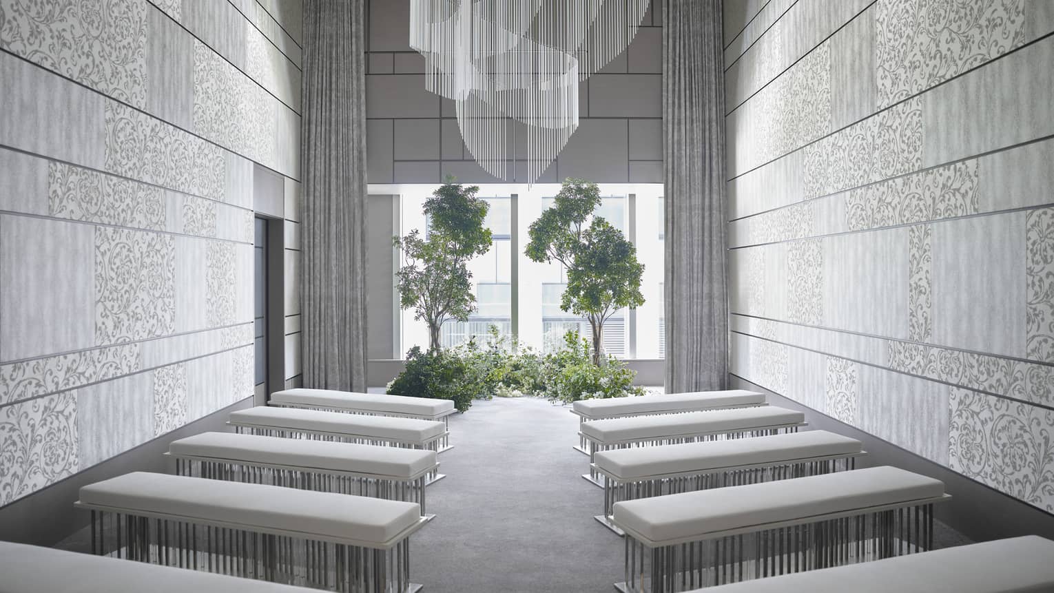Modern event room, rows of plush benches face window and potted trees
