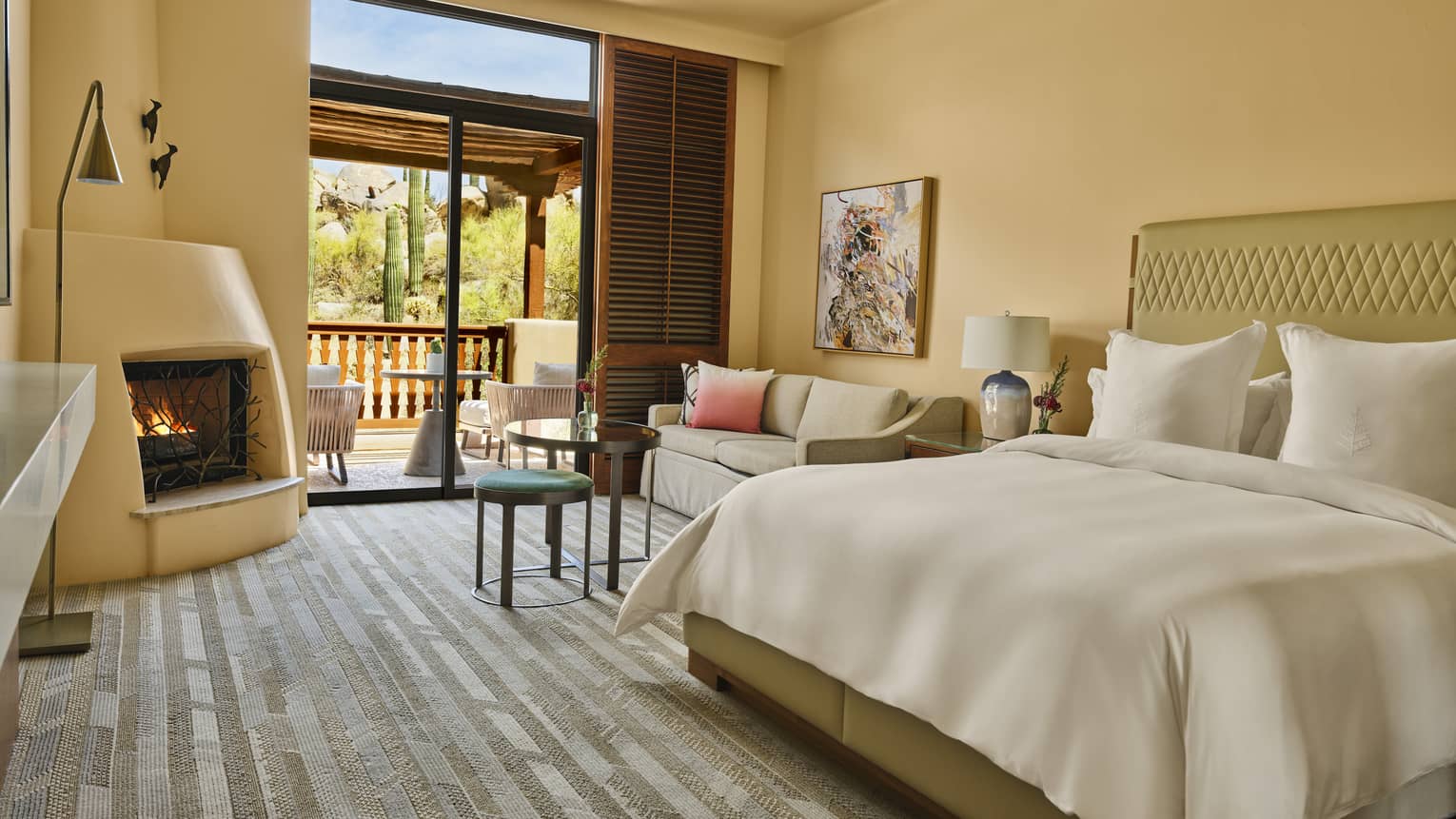 Resort guest room featuring king bed, seating area with small sofa, a kiva fireplace and a walk-out terrace
