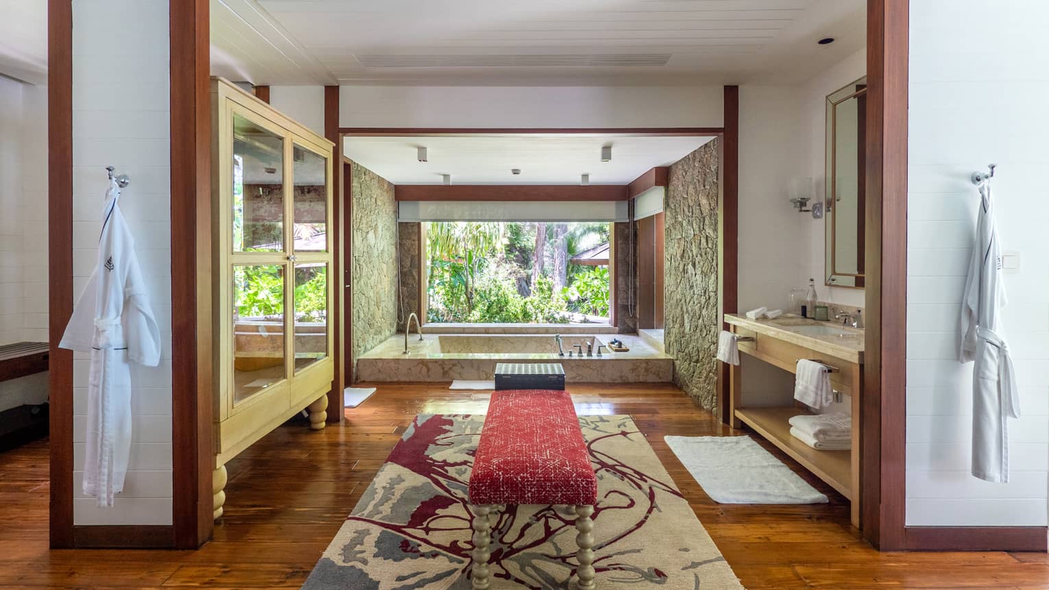 Lavish large bathroom with bench in the middle, sunken tub and window with tropical view