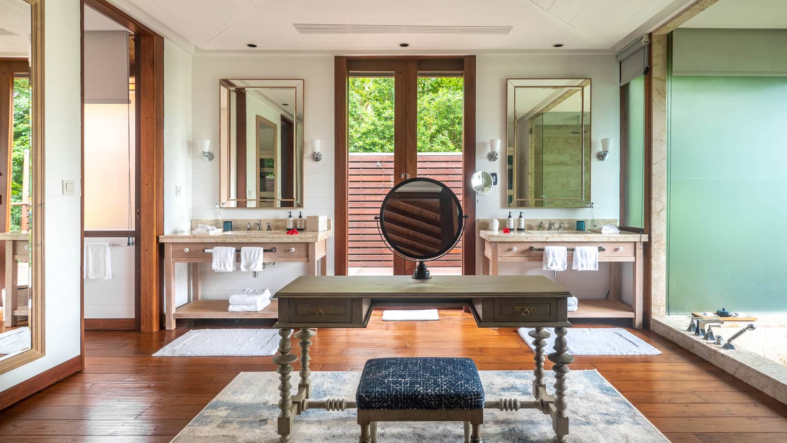Large bathroom with make-up vanity in the middle, area rug, two sink vanities and door to outdoor terrace