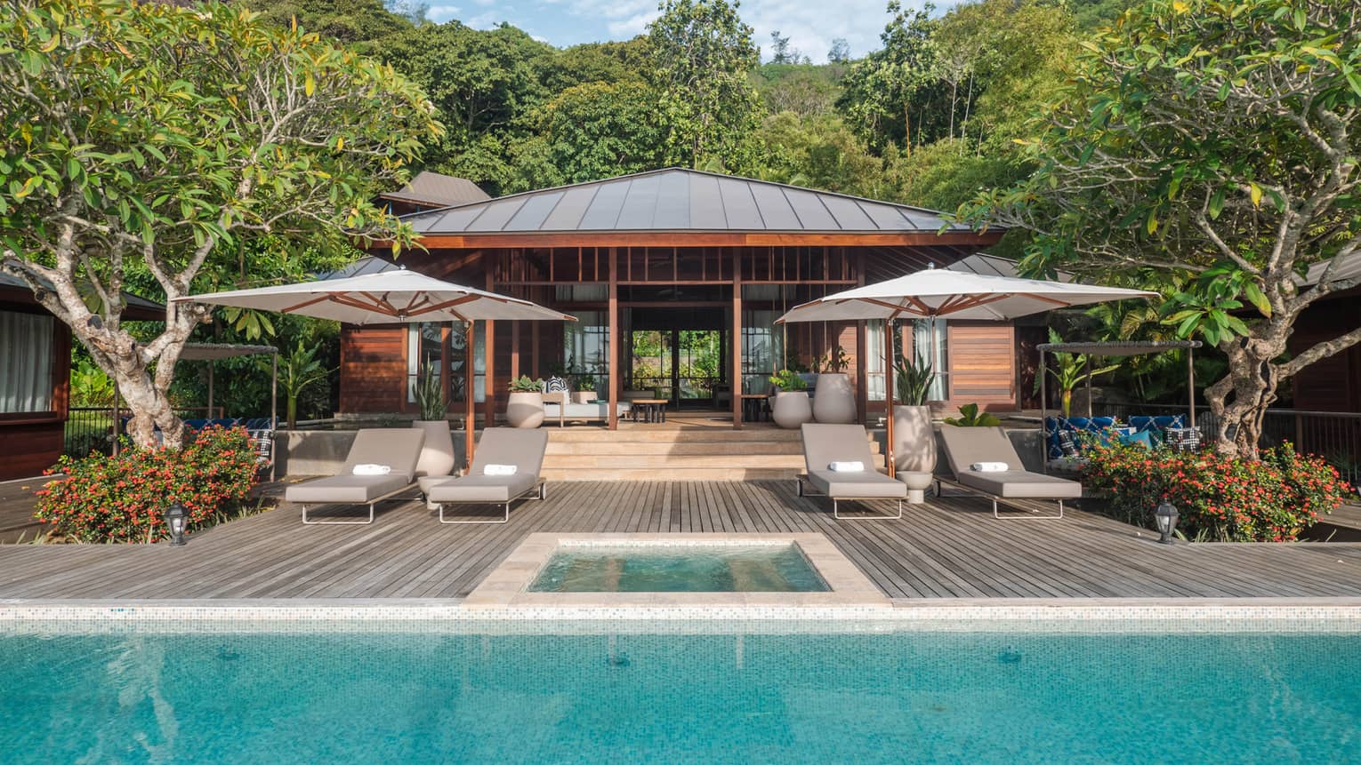 A private villa's pool terrace with four lounge chairs and two umbrellas
