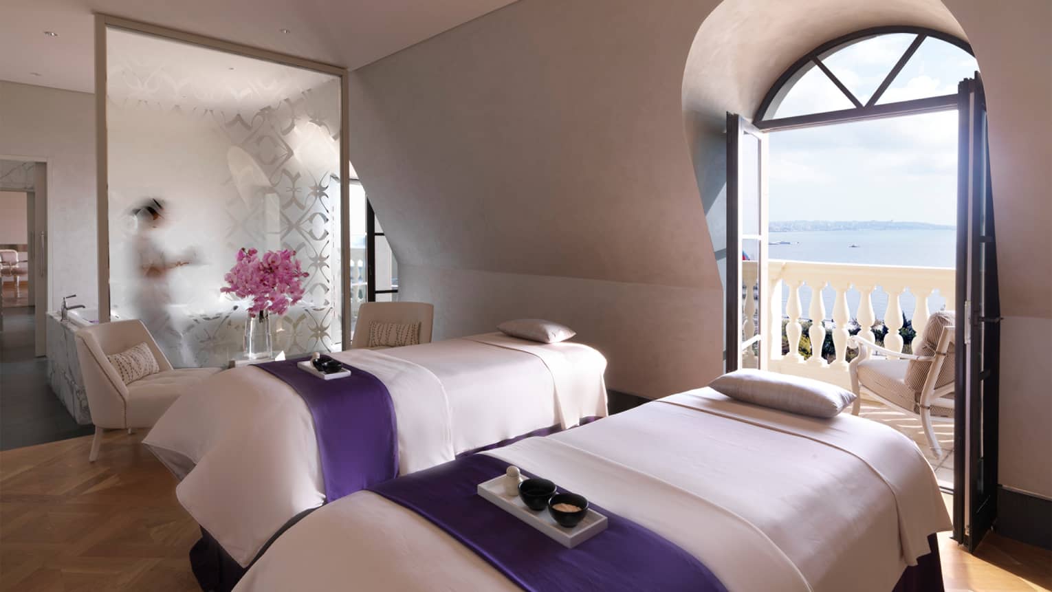 Spa with two massage beds by open balcony door overlooking ocean