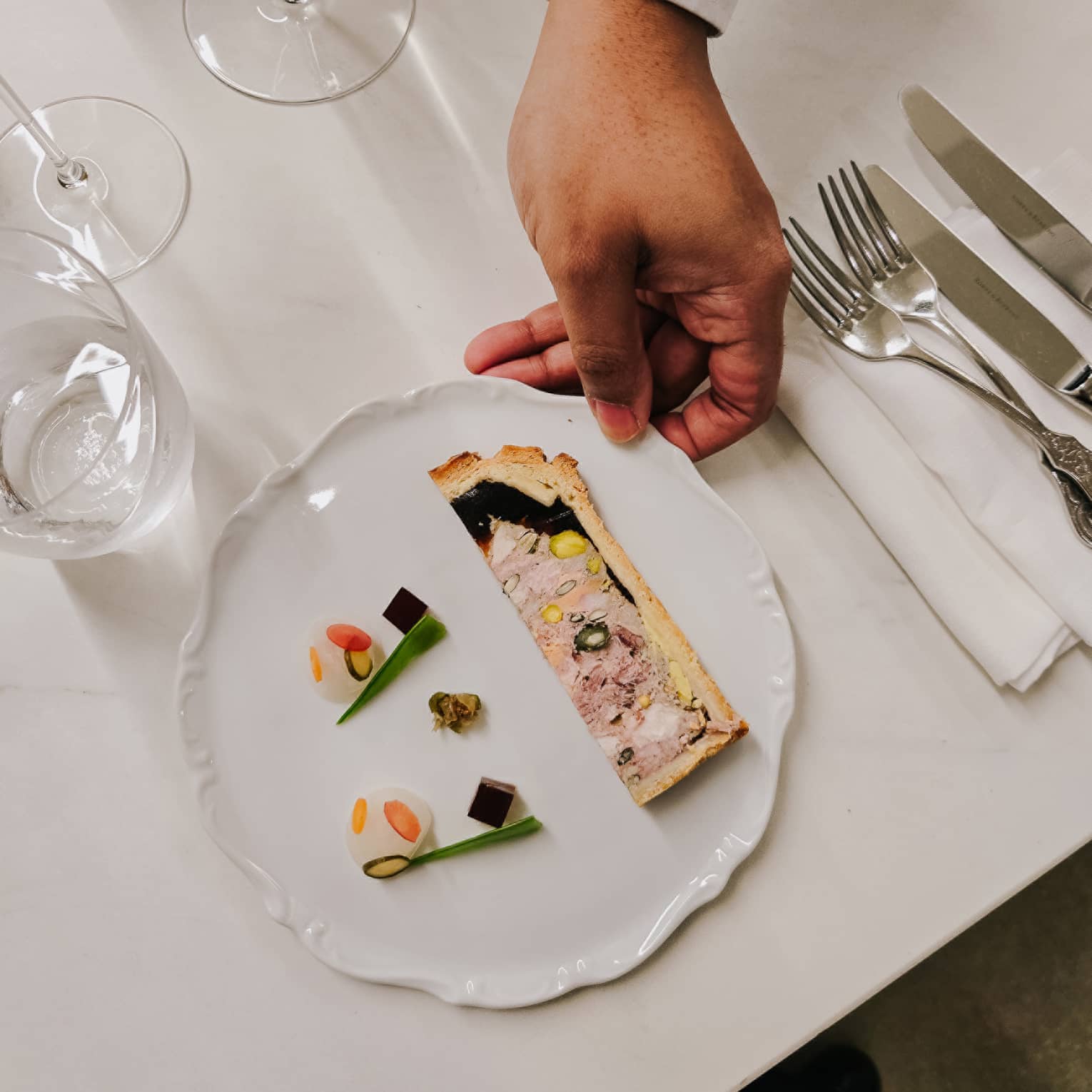 A culinary dish with silverware and wine glasses on the side