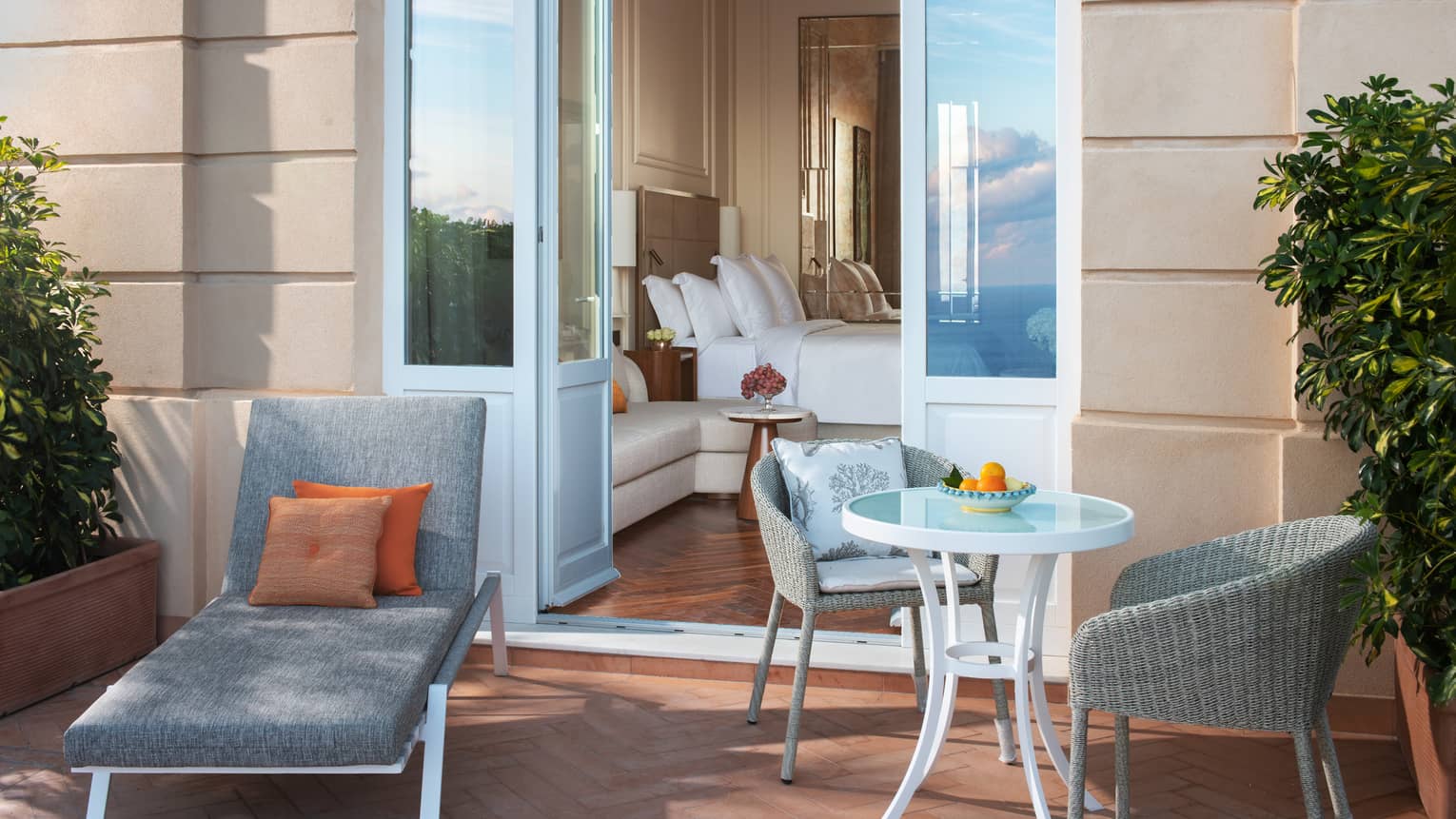 A hotel room balcony, with a lounge chair and small round table with two chairs