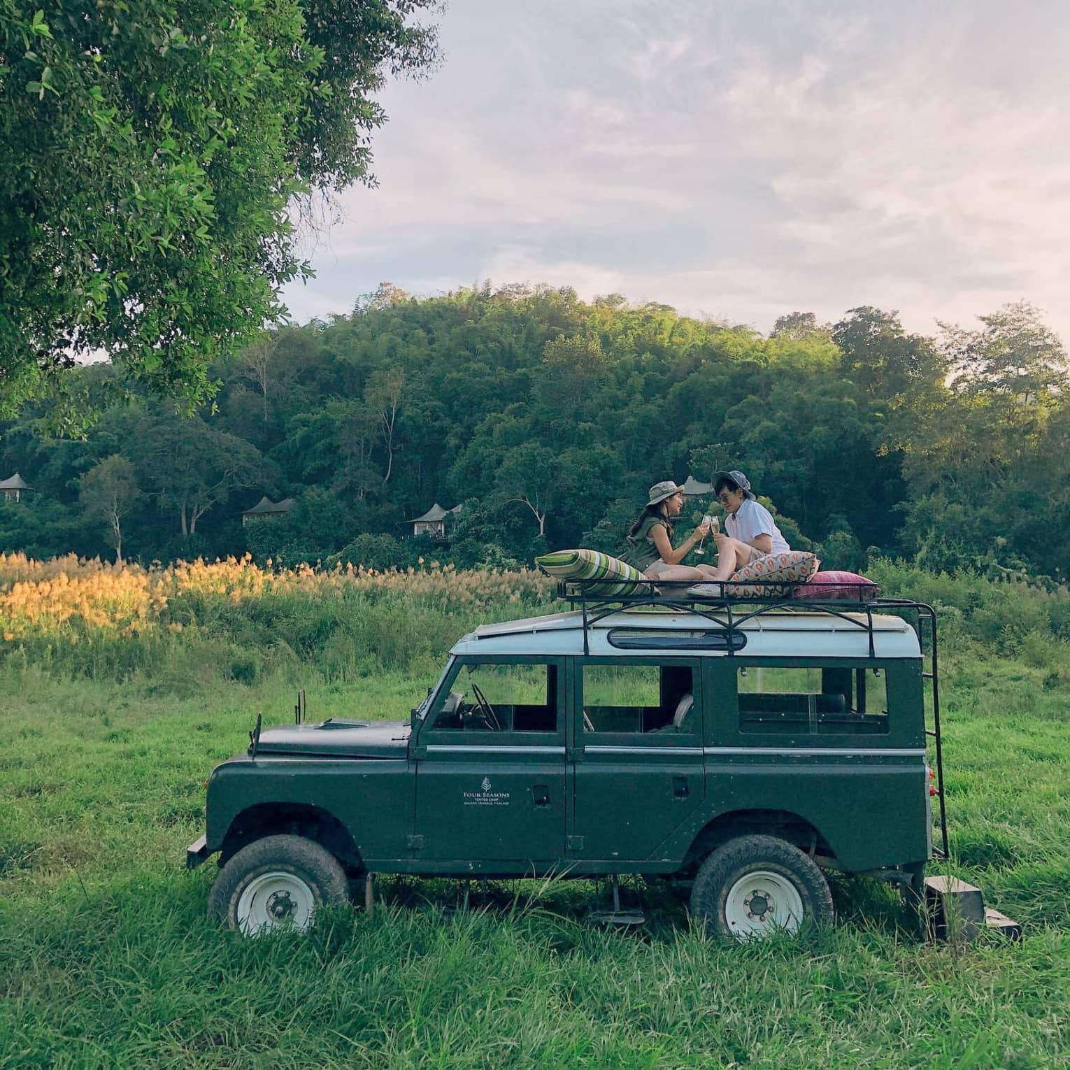 Two guests sit on top of a safari vehicle in a field