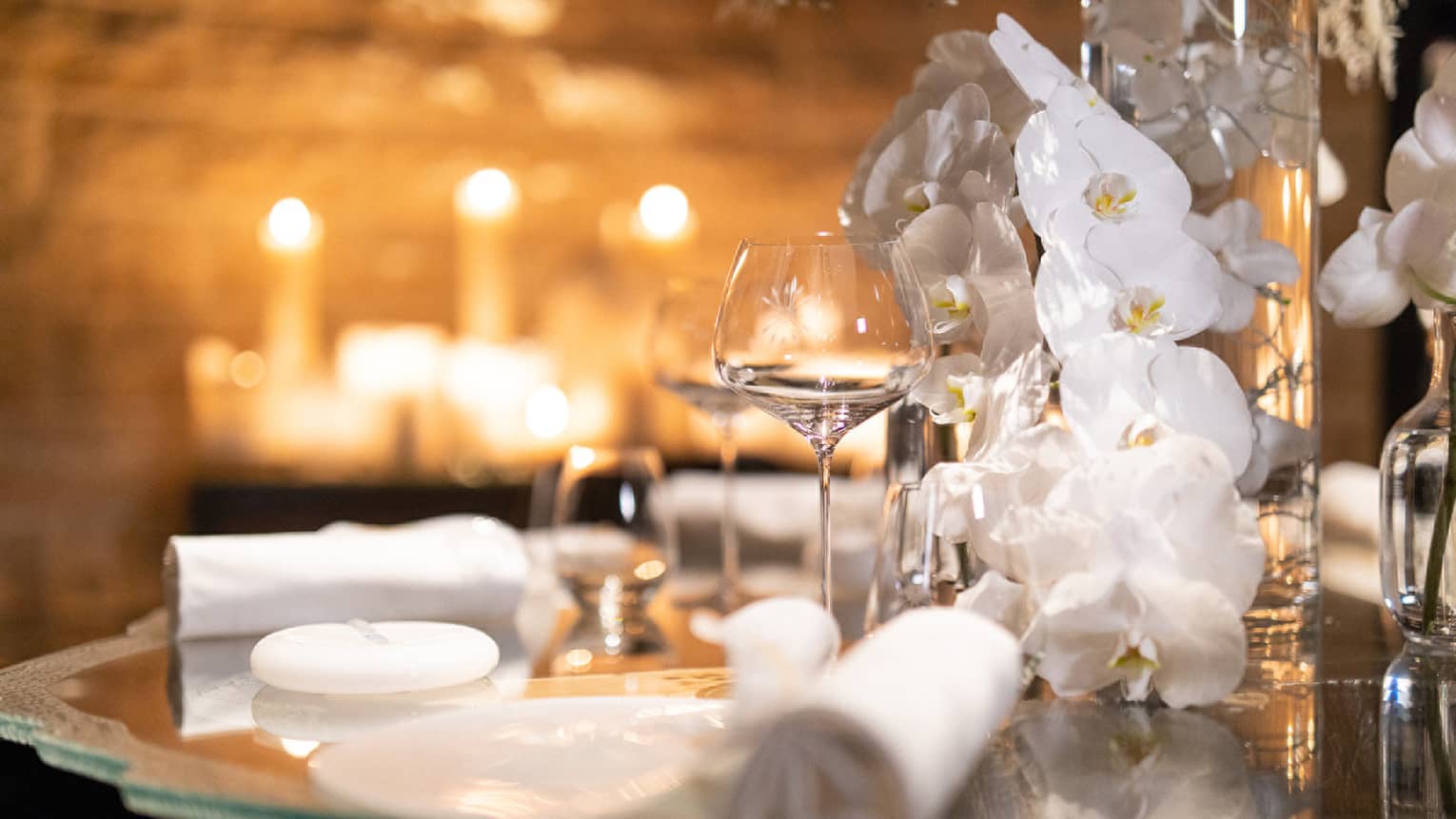 White orchids, rolled napkins and glassware on dining table in candle lit room
