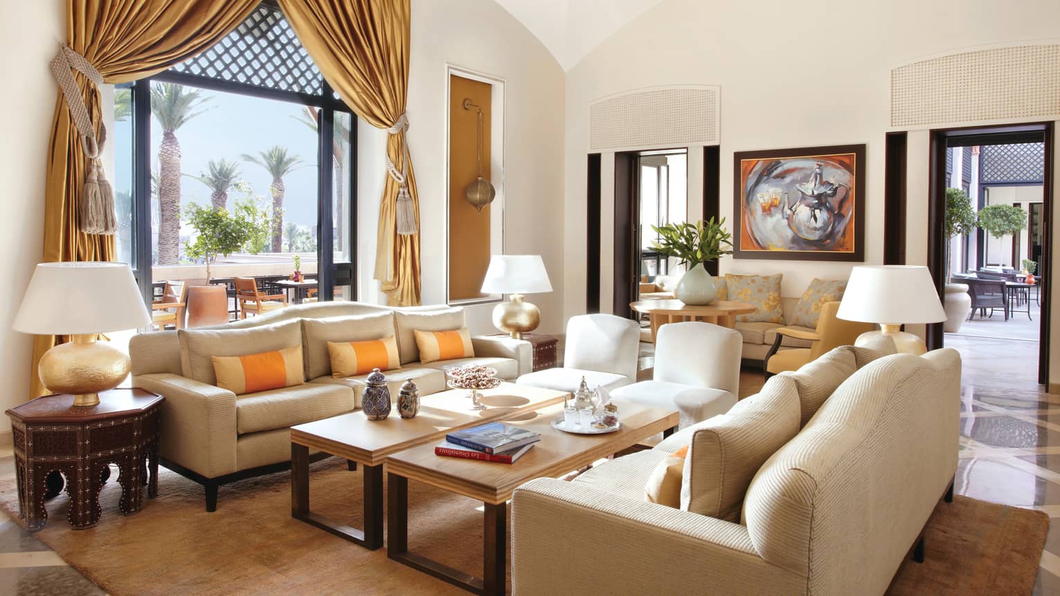 Sunny lounge area with two white sofas in front of light wood tables with books, trays, vases, large window