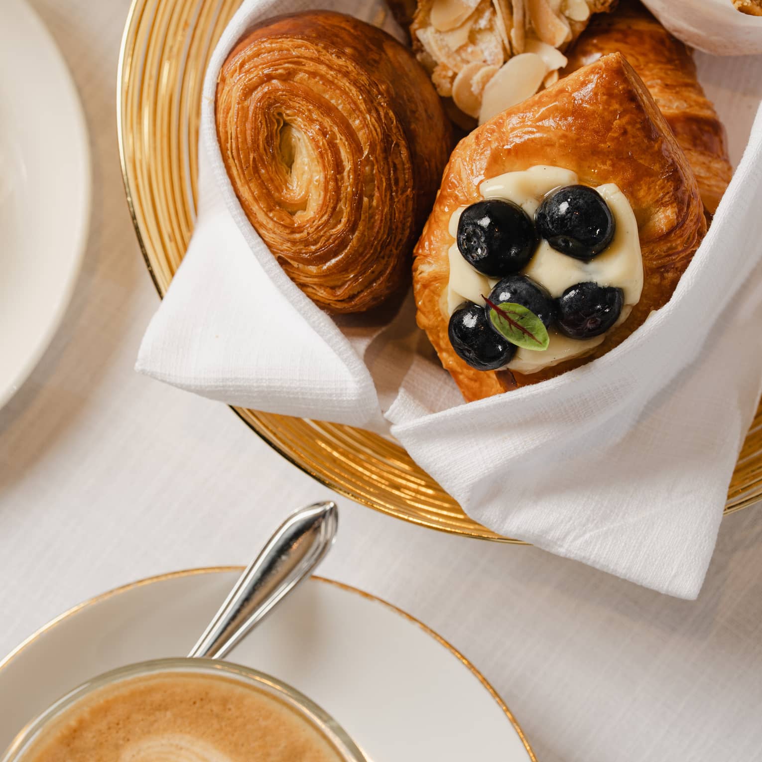Gold-rimmed bowl filled with breakfast pastries sits on a table next to a white mug of coffee