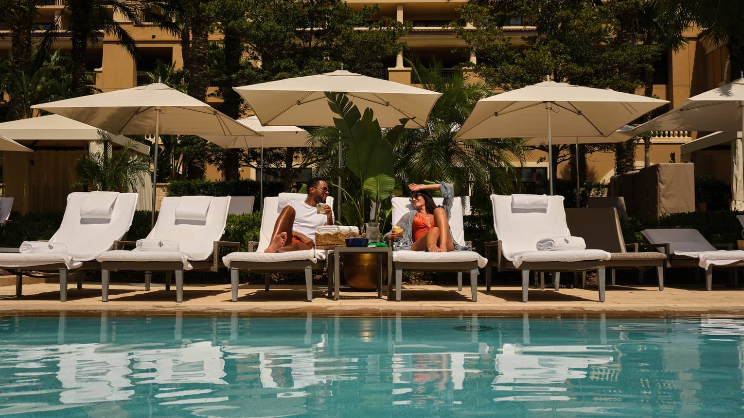 Two people lay on white lounge chairs next to a hotel pool