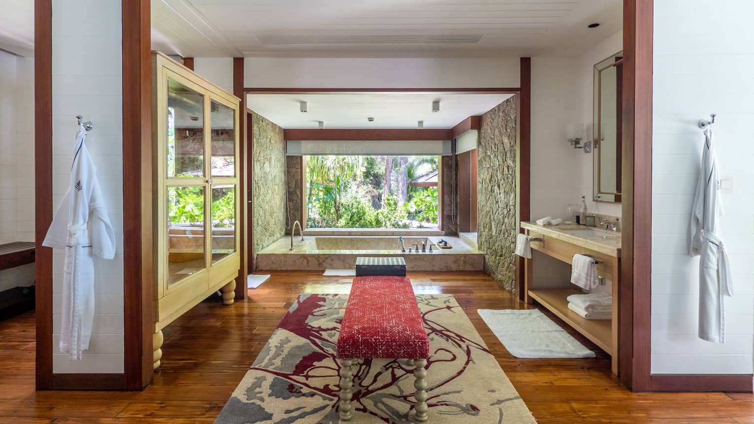 Lavish large bathroom with bench in the middle, sunken tub and window with tropical view
