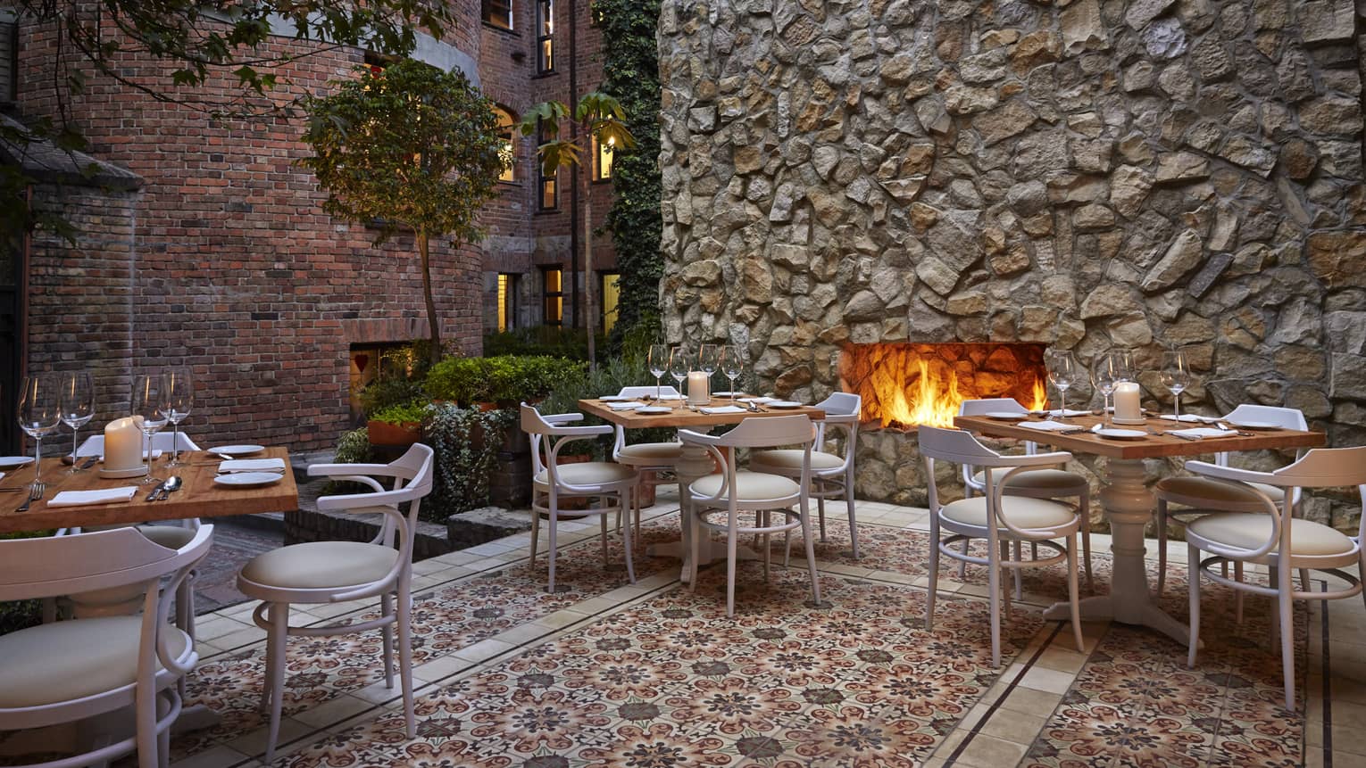 An outdoor patio with a fireplace, and several tables and chairs set up around.