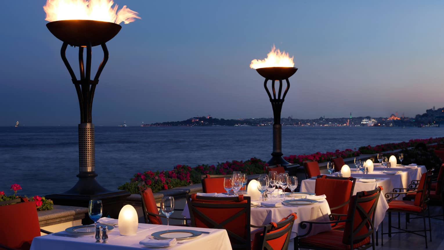 Tall torches between dining table on Aqua patio at dusk