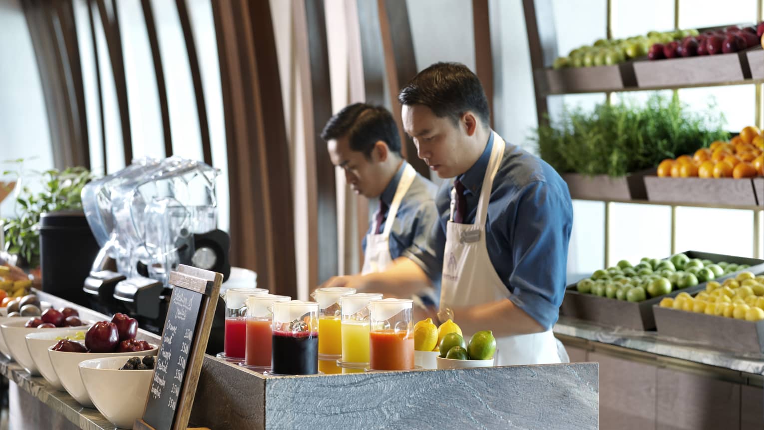 Two baristas standing at a counter in front of a tray of vegetables.