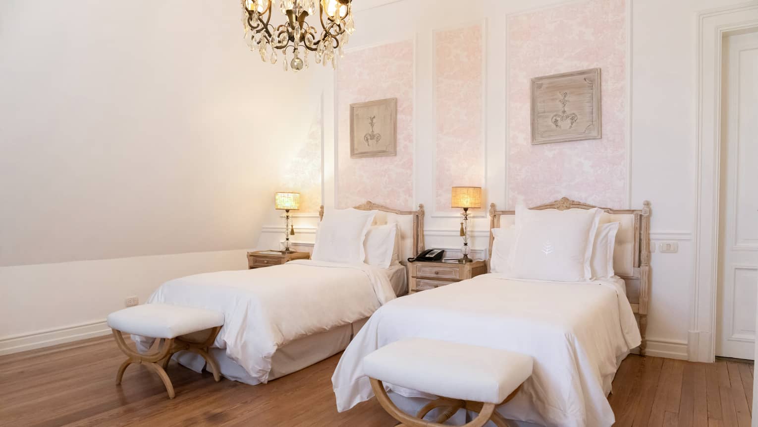 Two twin beds with white comforters in a room with a chandelier.