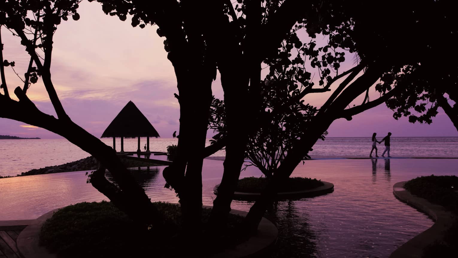 Serenity Pool winding around trees at sunset, silhouette of couple in background