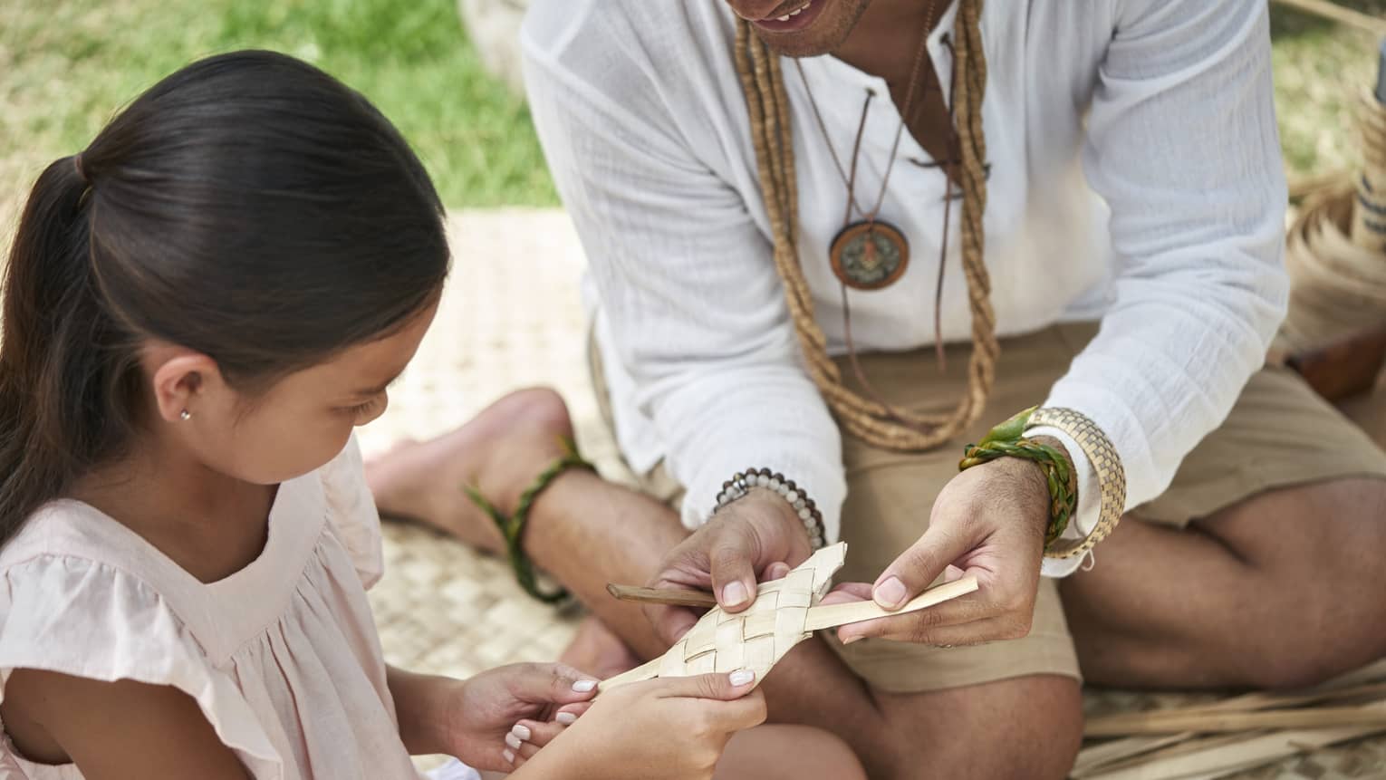 An adult shows a young girl how to weave a basket