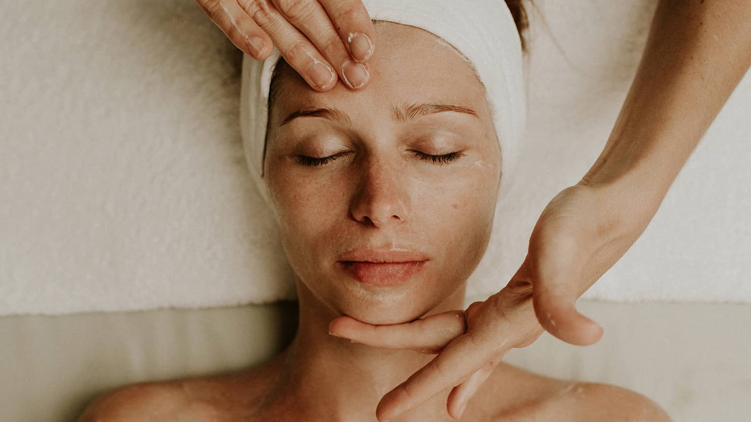 Person receiving a relaxing facial massage with eyes closed and head wrapped in a towel