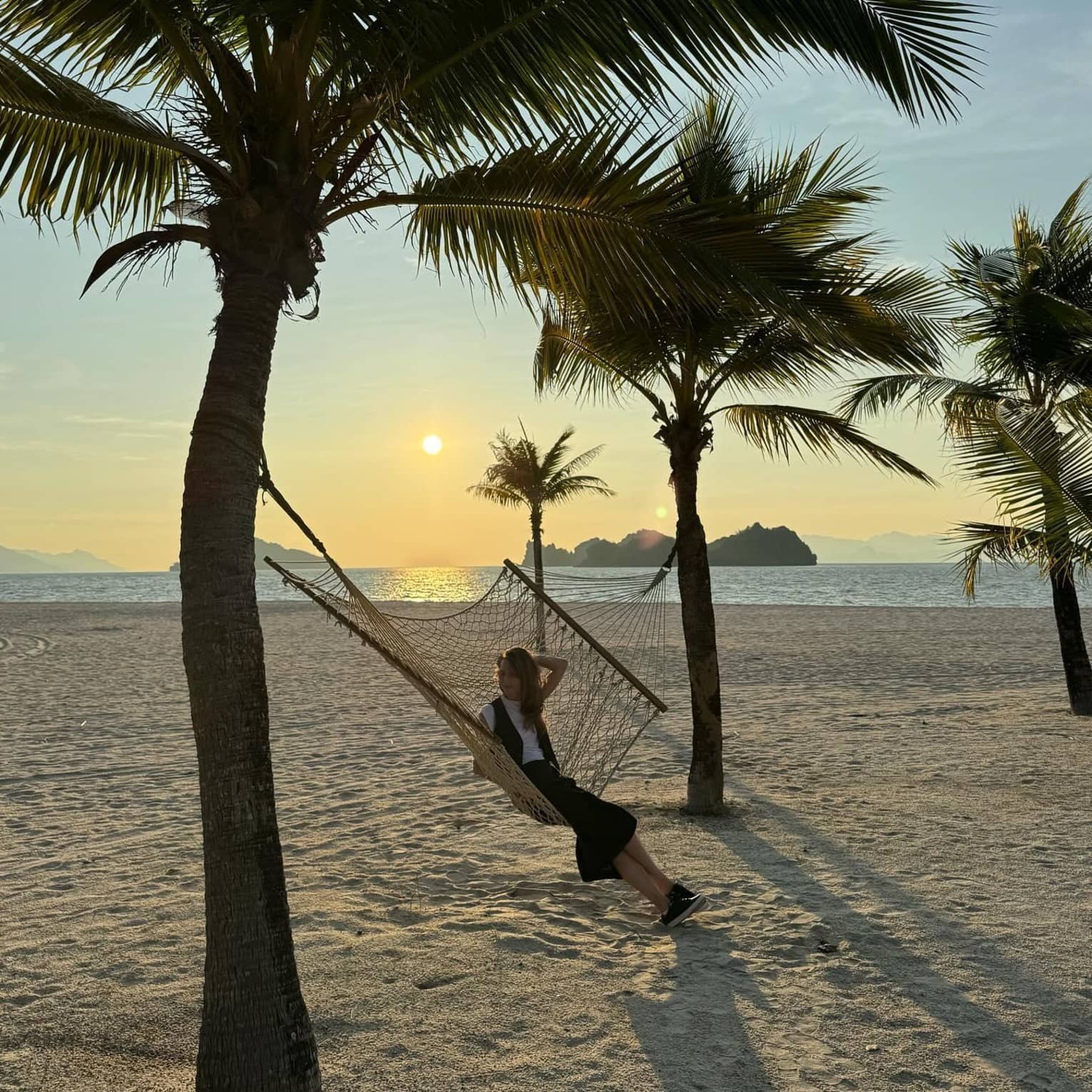 A guest relaxing in a hammock on a beach at sunset