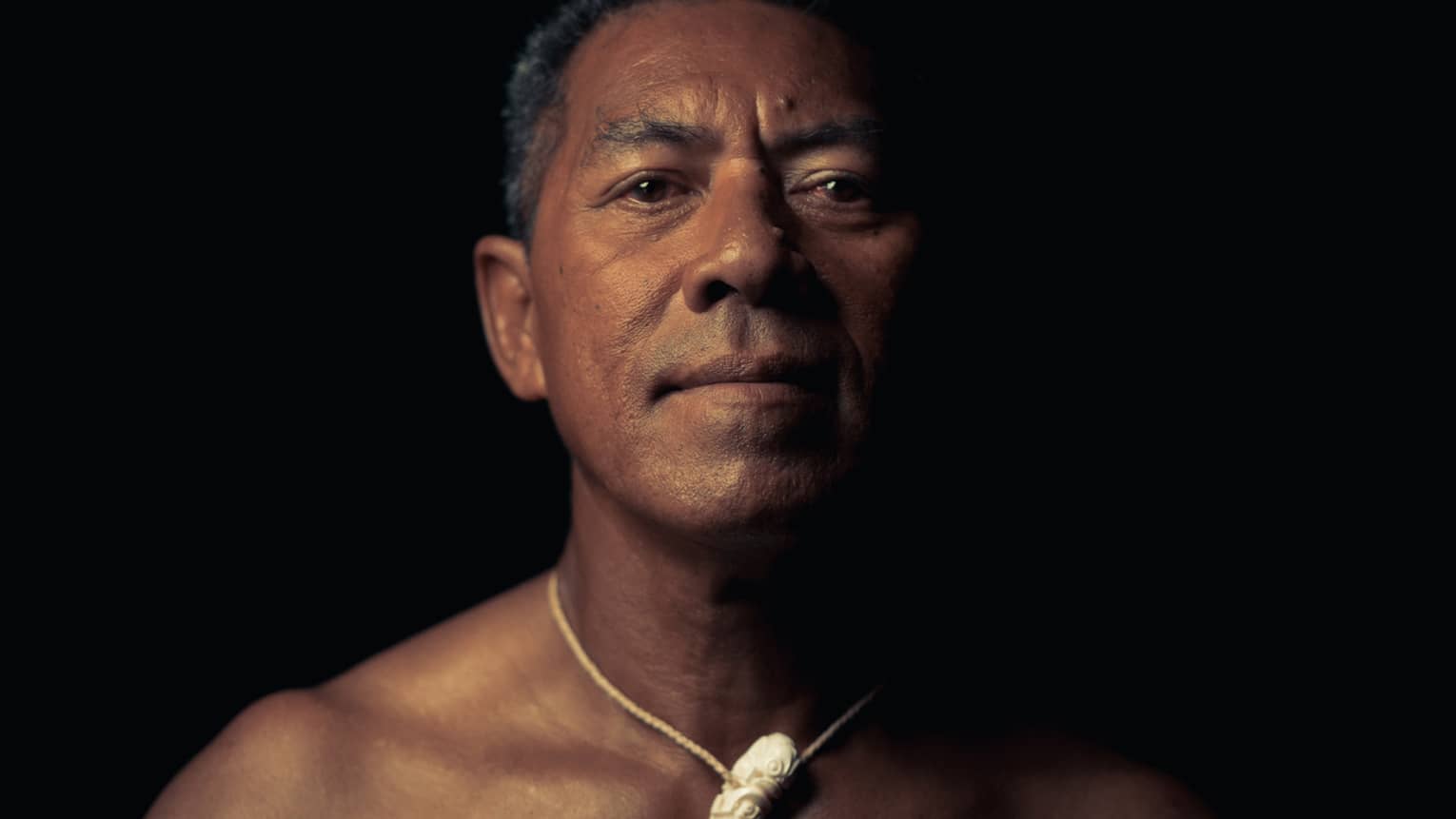 Person wearing a crescent-shaped necklace, standing against a dark background