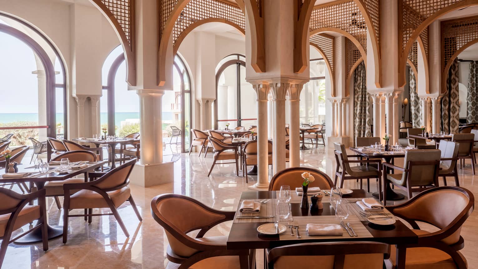 Restaurant dining area with archways, set square tables, tan leather dining chairs, water view
