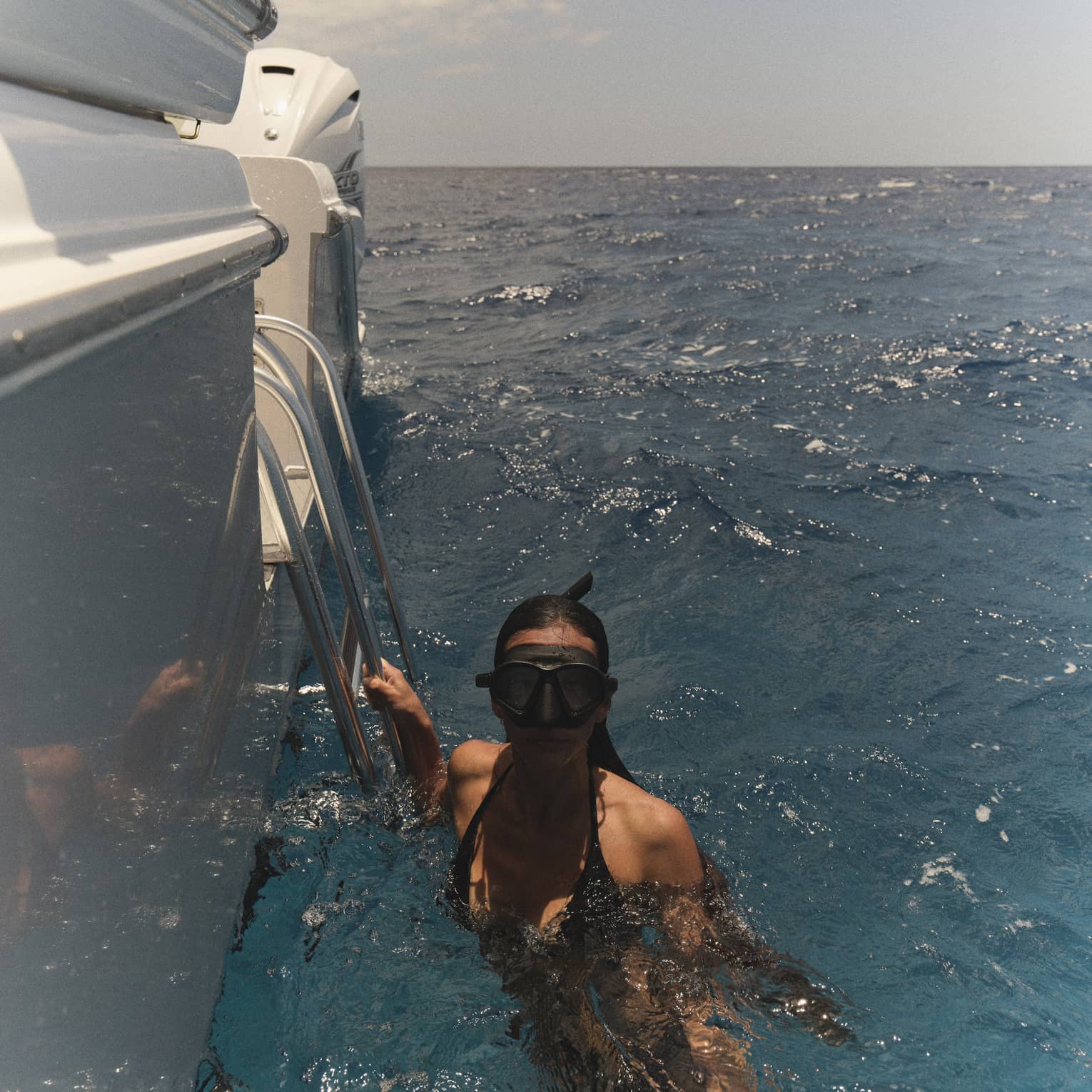 A woman wearing snorkelling goggles holds onto edge of boat in the water