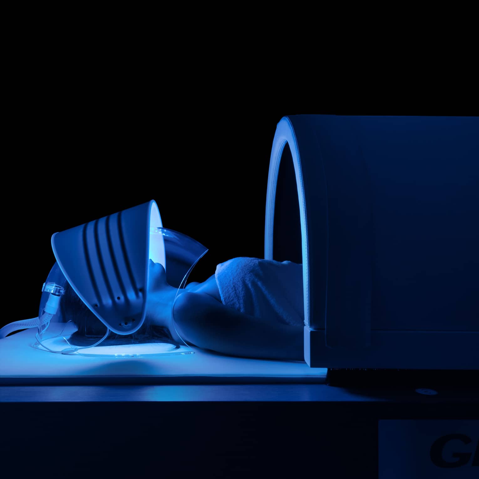 Person wears mask with blue lights under dome in dark spa room