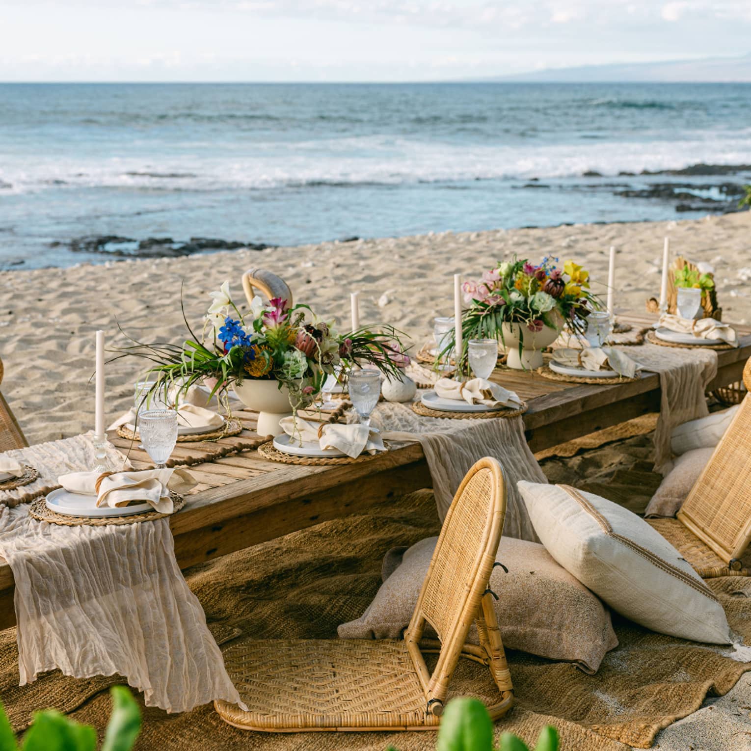 Low dining table set on the beach for an elaborate gourmet picnic, with floral arrangements and candle sticks