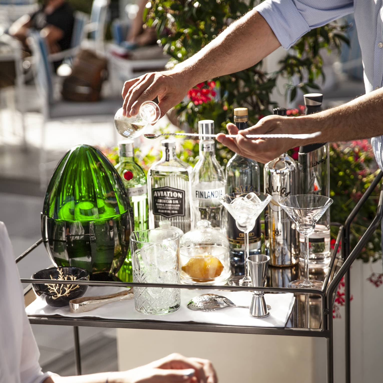 Man pours a drink at outdoor cocktail service cart with various glass bottles