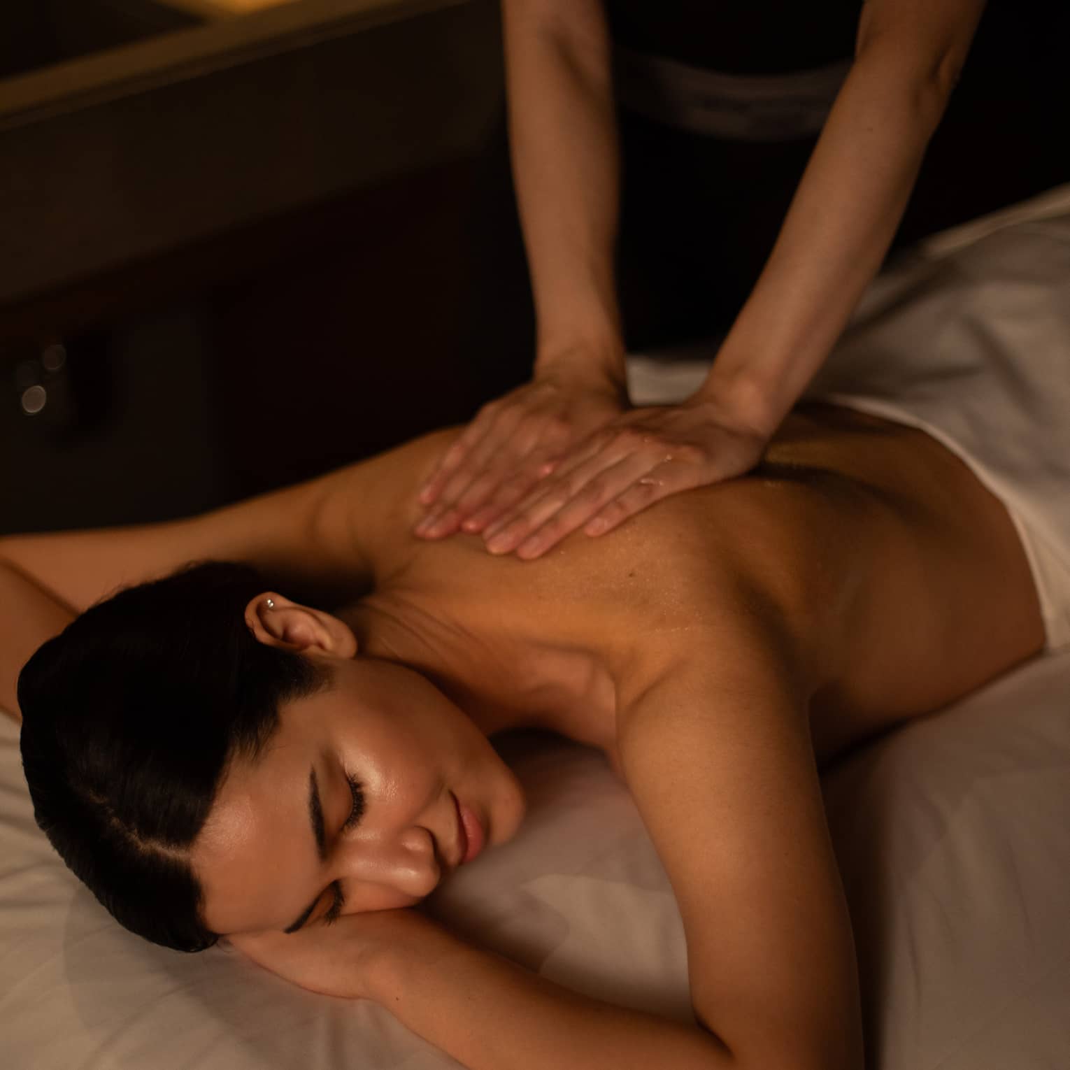 A woman receiving a massage in a dimly lit treatment room.