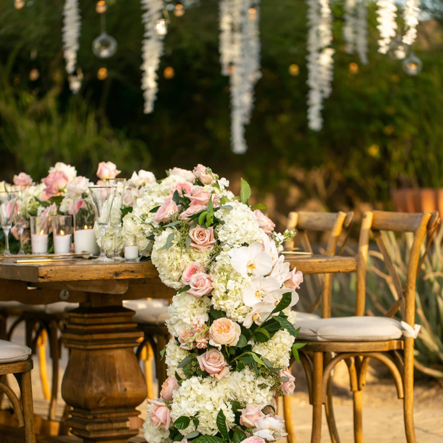 Outdoor chairs and table with a large bouquet of pink roses and candles.