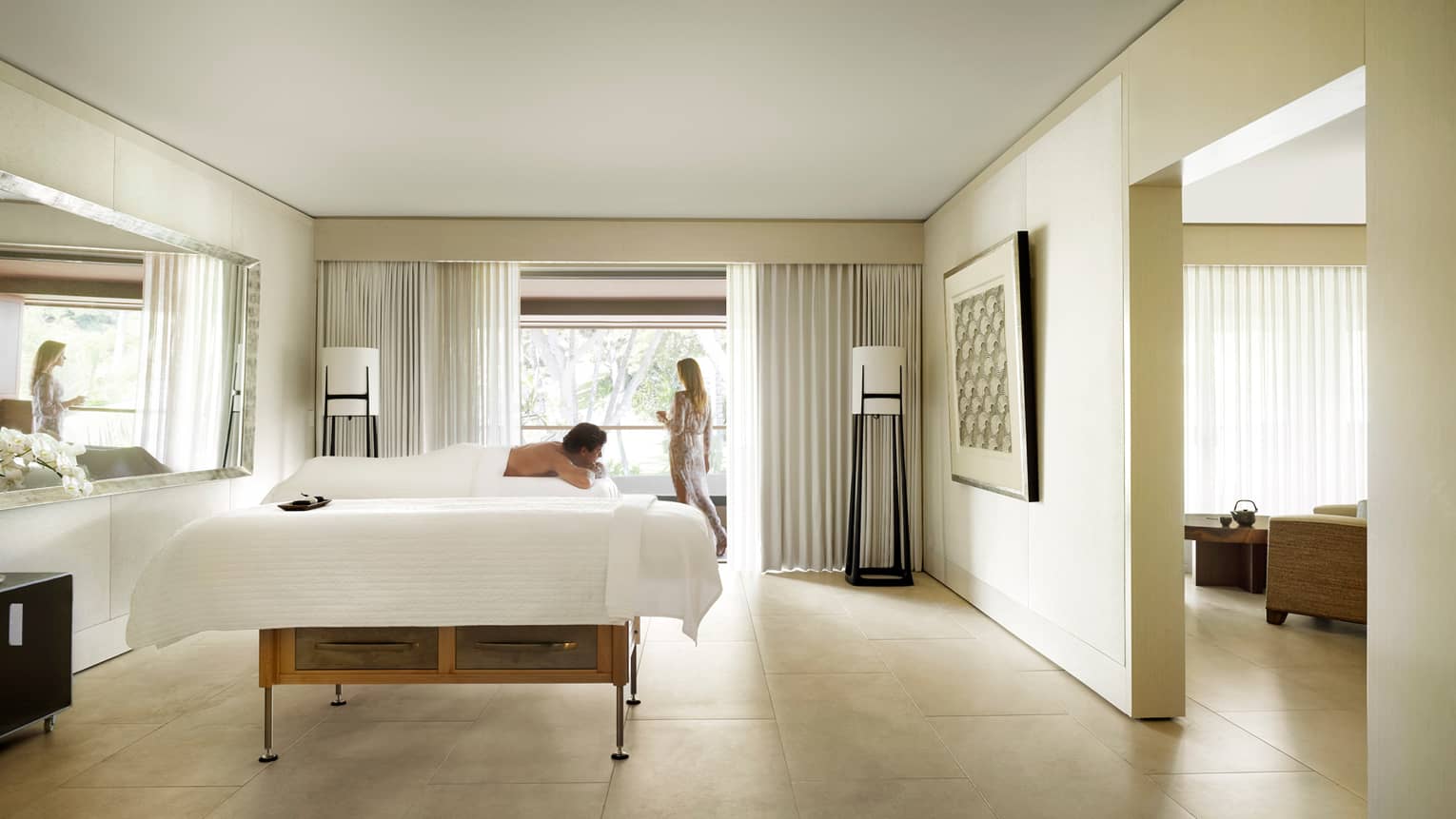 Woman at window, man lies on massage table in Couples Suite in spa