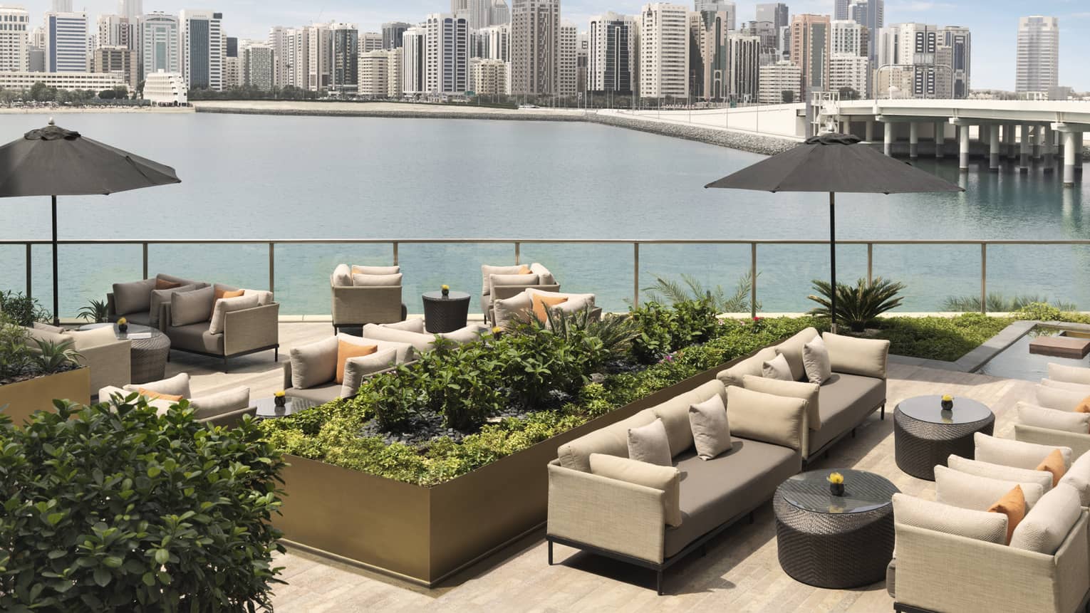 Outdoor sofas, umbrellas and planters on patio overlooking water, city