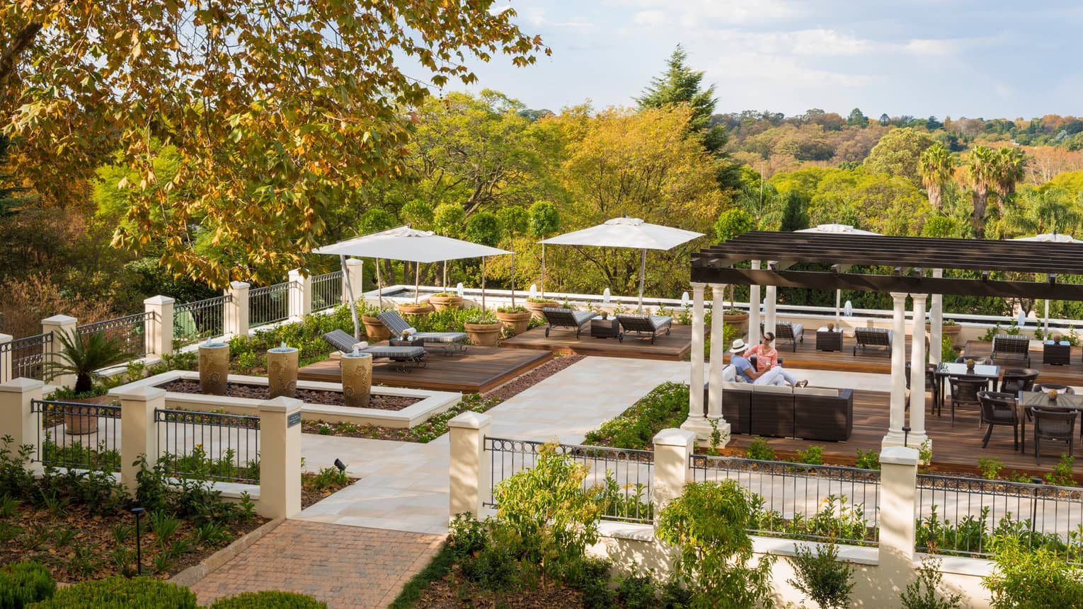 Looking down at iron fence around outdoor patio and courtyard with lounge chairs, people under pergola