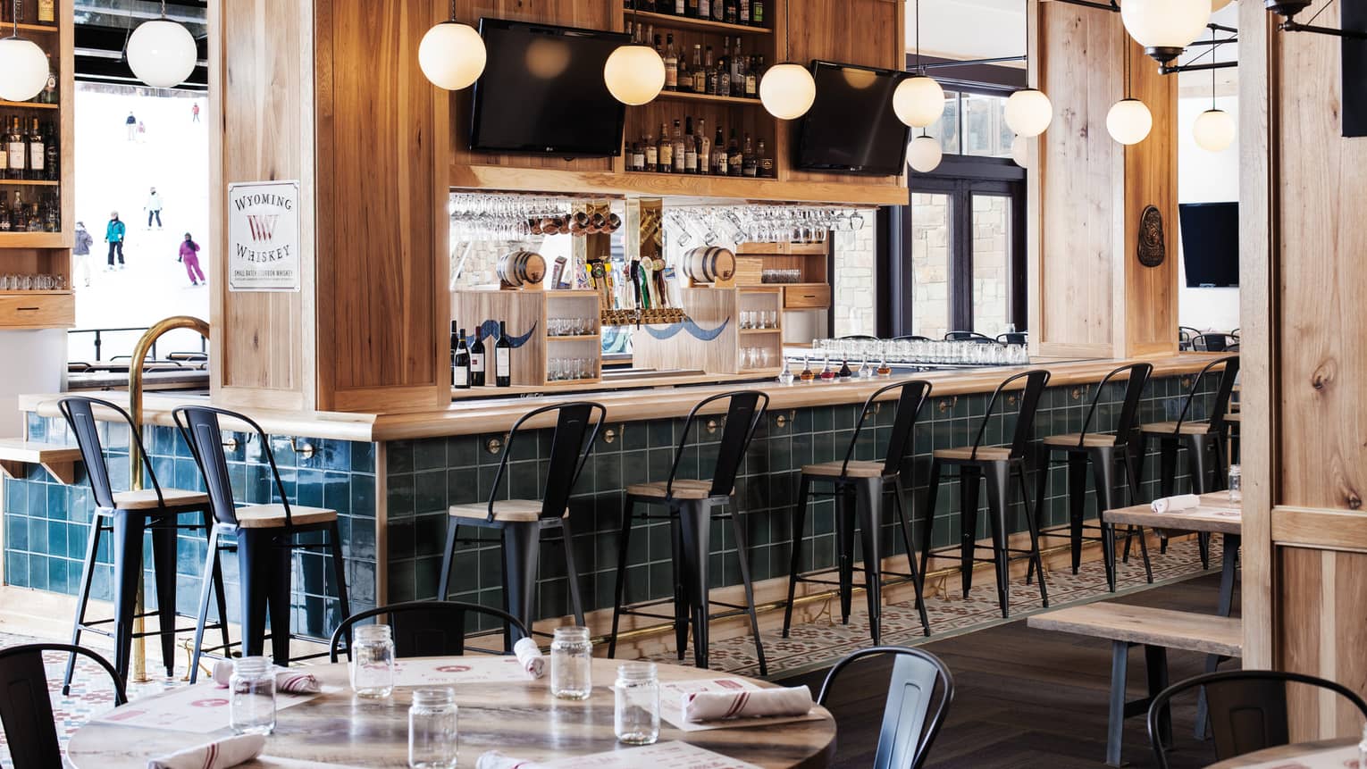 High chairs are positioned around a bar, bright windows show guests skiing outside