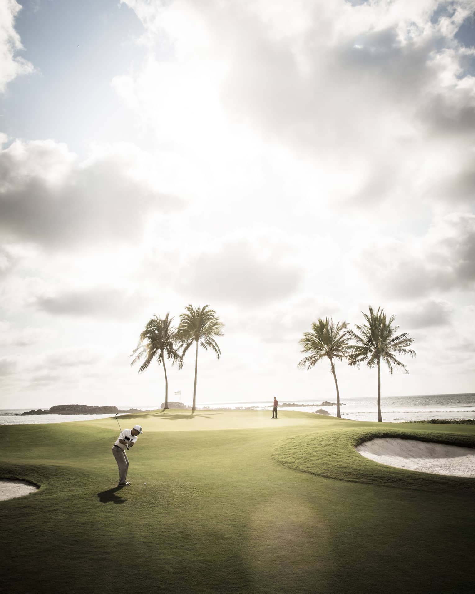 Man swings golf club on sunny course green with four palm trees