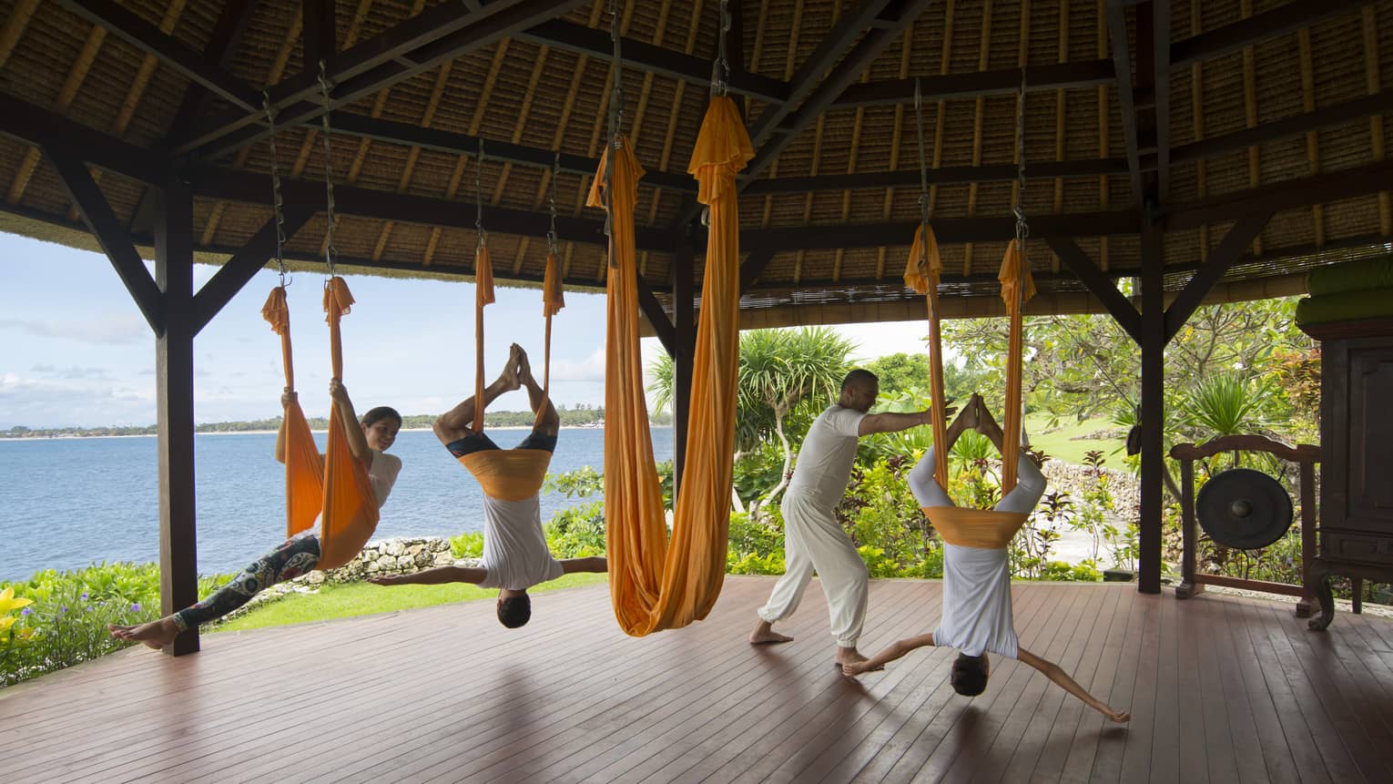 Guests hang from the ceiling as they are guided through rope yoga in an outdoor pavilion