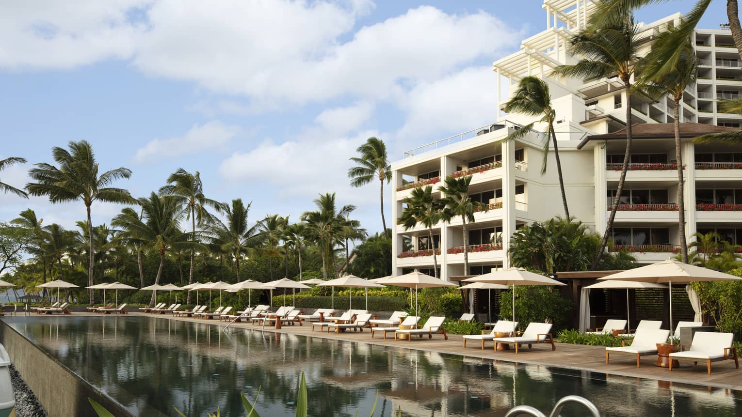 Exterior building and outdoor pool lined with white lounge chairs at tropical Resort