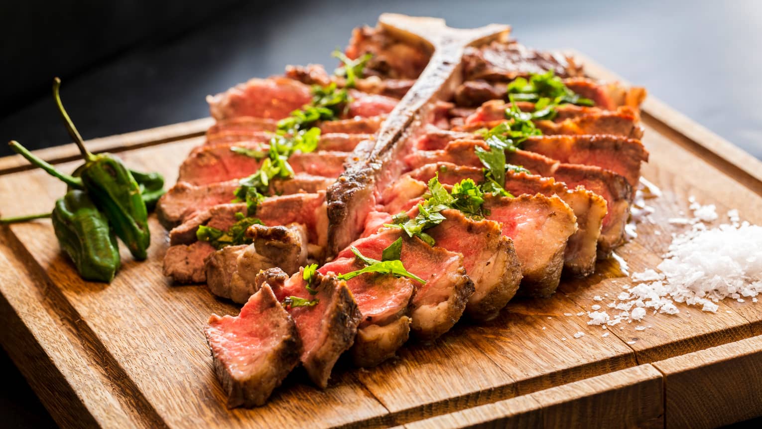 Porterhouse Steak slices of beef on wood butcher's board with green jalapeno peppers