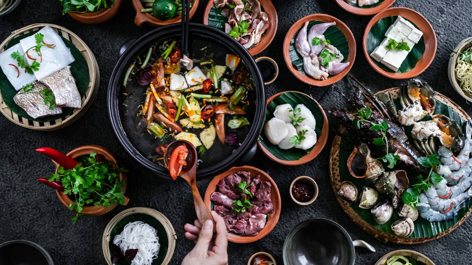 Aerial view of bowls filled with Vietnamese dishes against black surface, hand holding wooden spoon