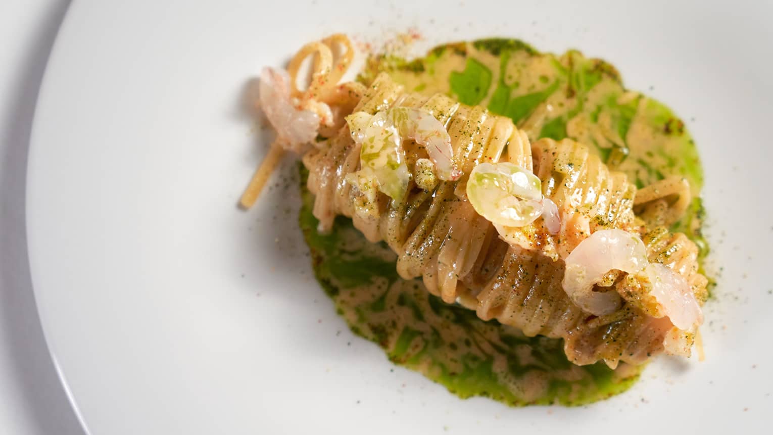 A round white plate holds a food item with sauce and garnishes.