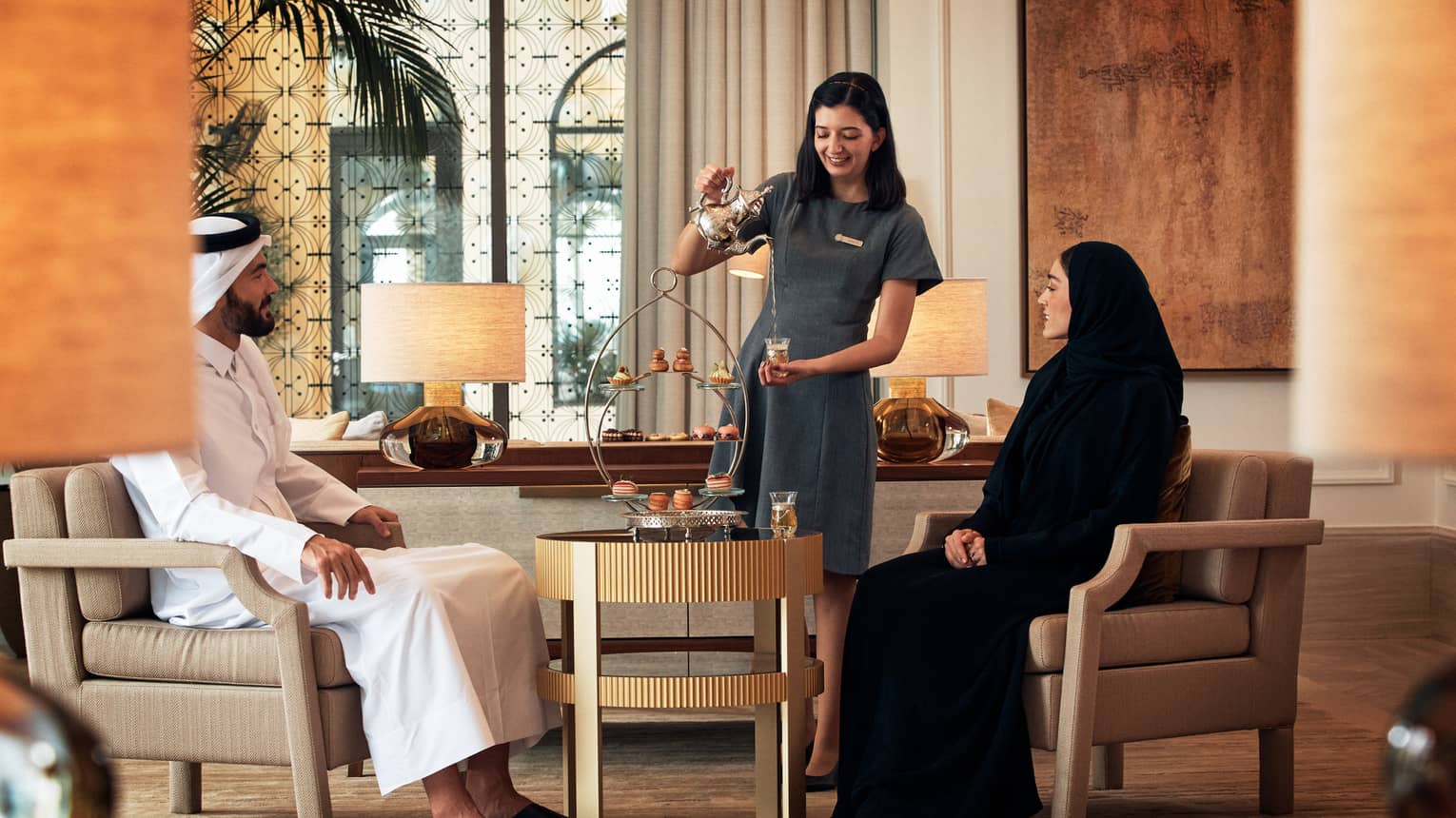 Woman serves afternoon tea to two people in luxury hotel lounge