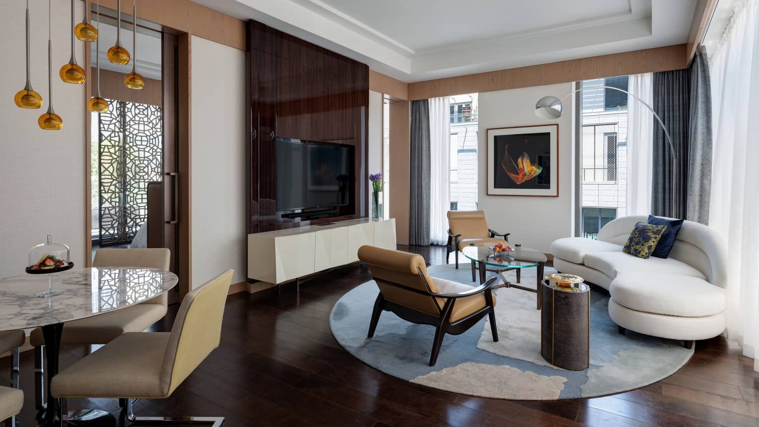 Living room with large TV, white curved sofa, two leather arm chairs, dining table