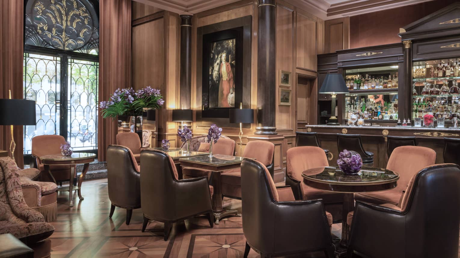 Bar with brown leather barstools and lounge area with rust-colored club-style seating, black lamps and purple flower arrangements