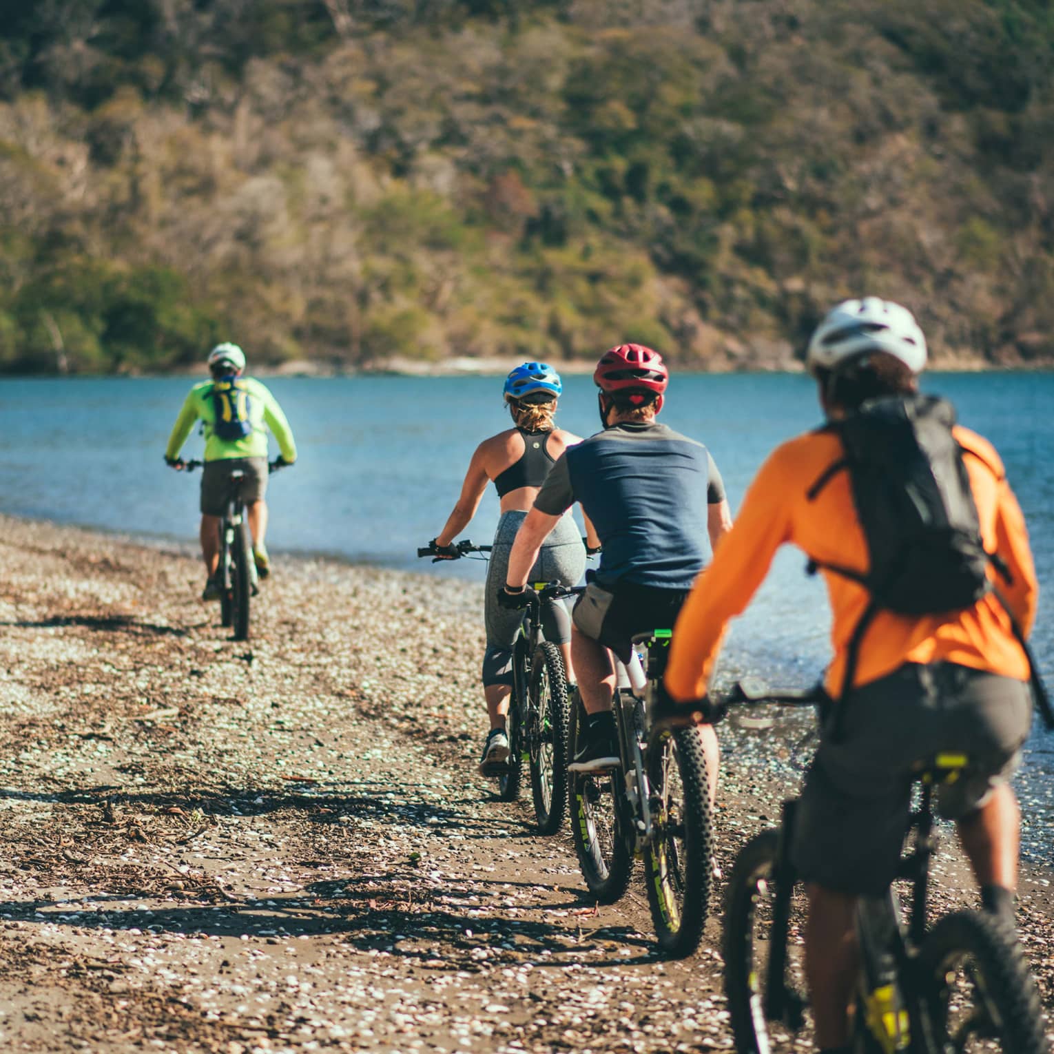 Four people riding bicycles through a rocky terrain next to the ocean